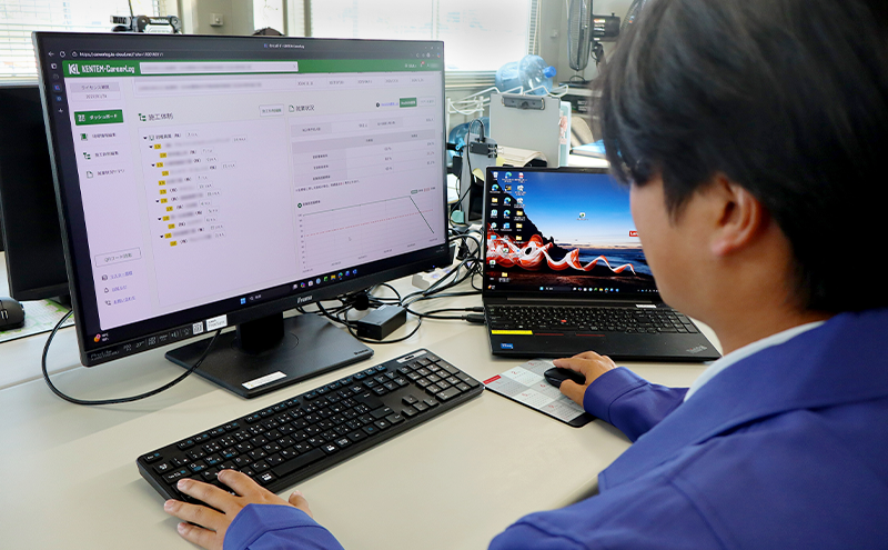 青い作業服を着た男性（松崎氏）がパソコンで「KENTEM-CareerLog」を操作している様子
