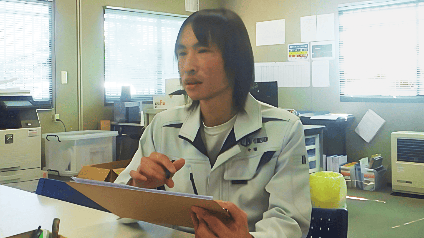 屋内でタブレットを操作している作業着の男性の写真。