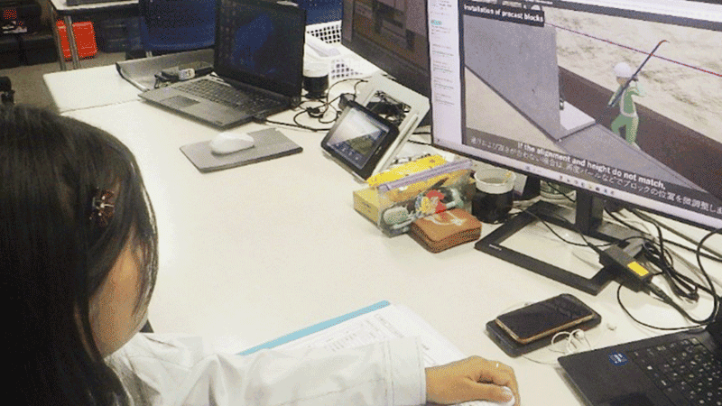 作業着の女性がモニターで動画を見ている様子。