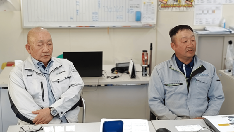 作業服を着た男性二人が並んでインタビューを受けている様子