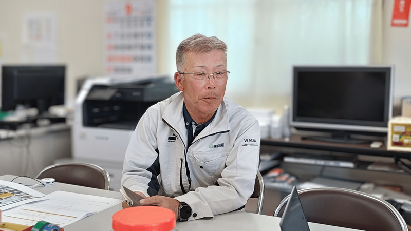 作業服を着た眼鏡の男性がインタビューを受けている様子