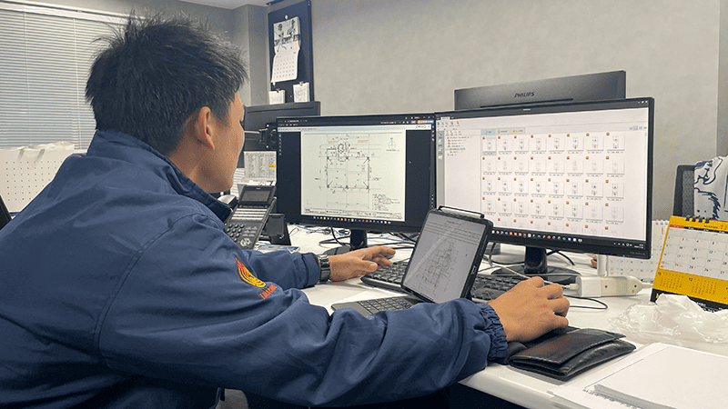 屋内でパソコンを操作する作業服の男性の写真