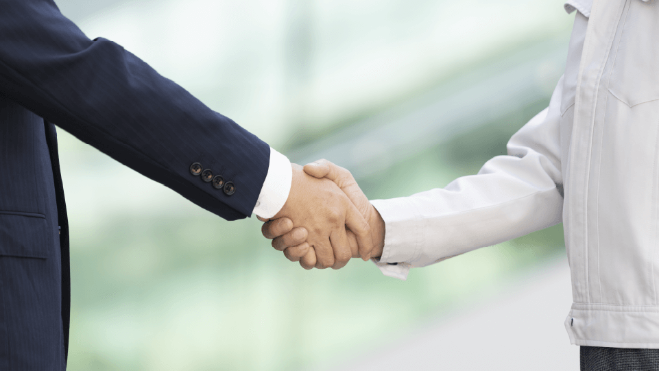 スーツを着た人と作業着の人が握手を交わしているイメージ写真